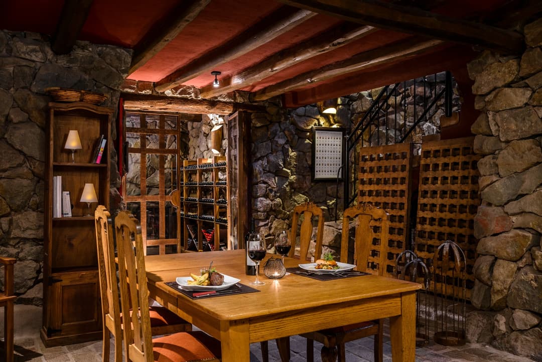 Cava subterránea de piedra con estanterías de vino y una mesa puesta para la cena